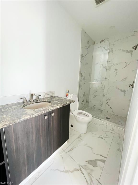 Bathroom featuring vanity, a marble finish shower, and light marble finish floors