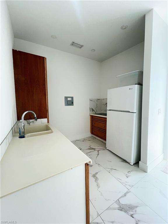 Kitchen featuring wood finish cabinets, light marble finish floors, freestanding refrigerator, and light countertops