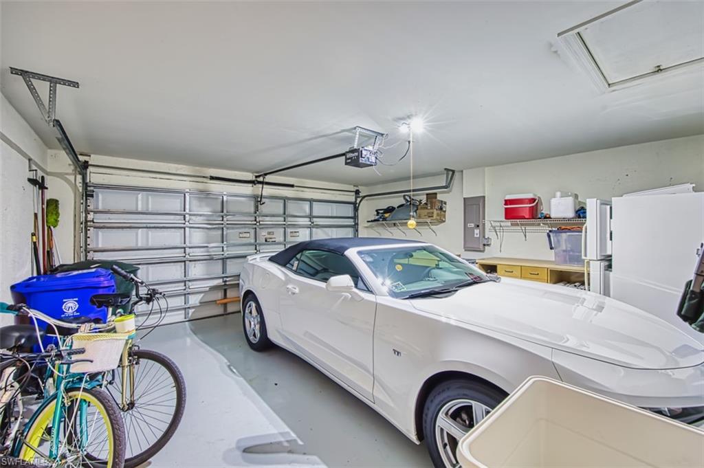 Garage featuring electric panel, freestanding refrigerator, and a garage door opener