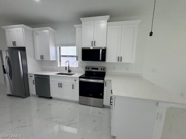 Kitchen featuring a peninsula, appliances with stainless steel finishes, light marble finish flooring, white cabinetry, and light stone counters