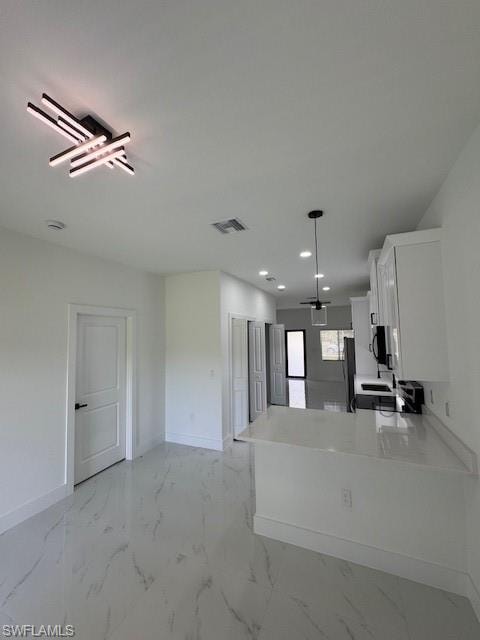 Kitchen featuring white cabinets, light marble finish floors, light stone counters, decorative light fixtures, and recessed lighting