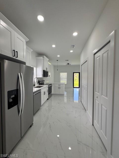 Kitchen featuring refrigerator, white cabinetry, light marble finish floors, range, and recessed lighting