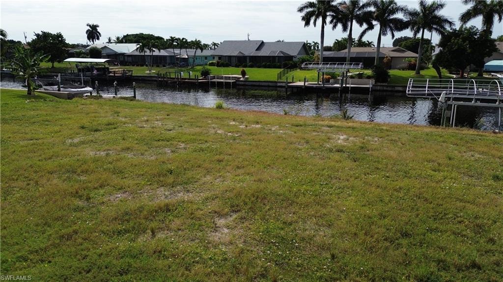 View of grassy yard with a dock, a water view, and a residential view