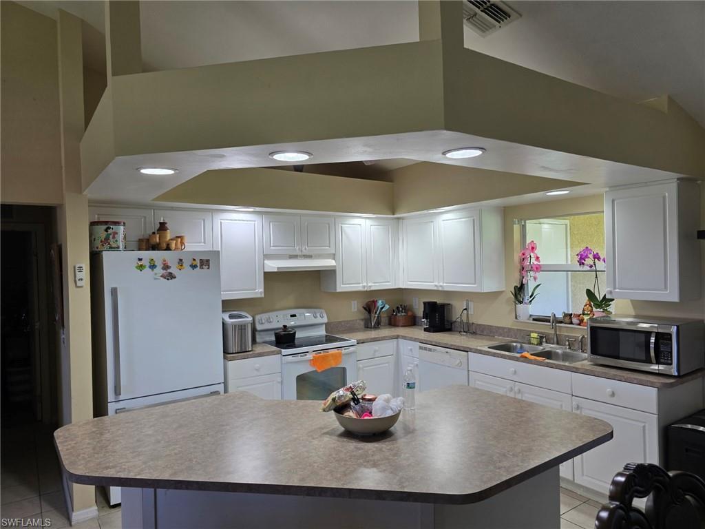 Kitchen with white cabinets, light tile patterned flooring, white appliances, a kitchen island, and under cabinet range hood