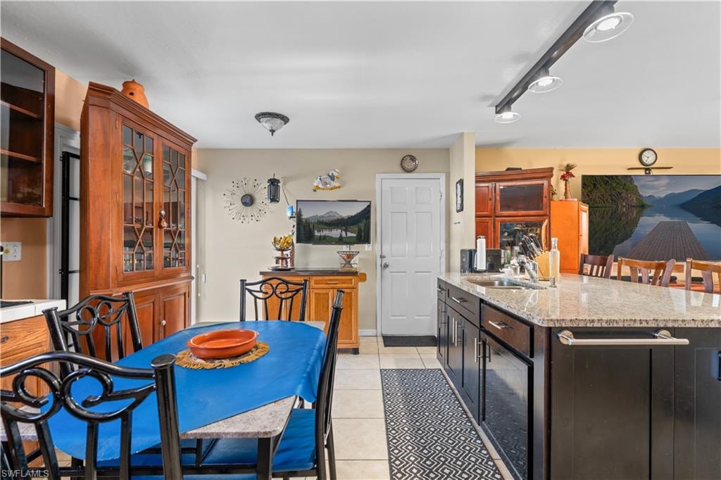 Kitchen featuring light tile patterned floors, light stone countertops, a center island with sink, glass insert cabinets, and dark brown cabinets