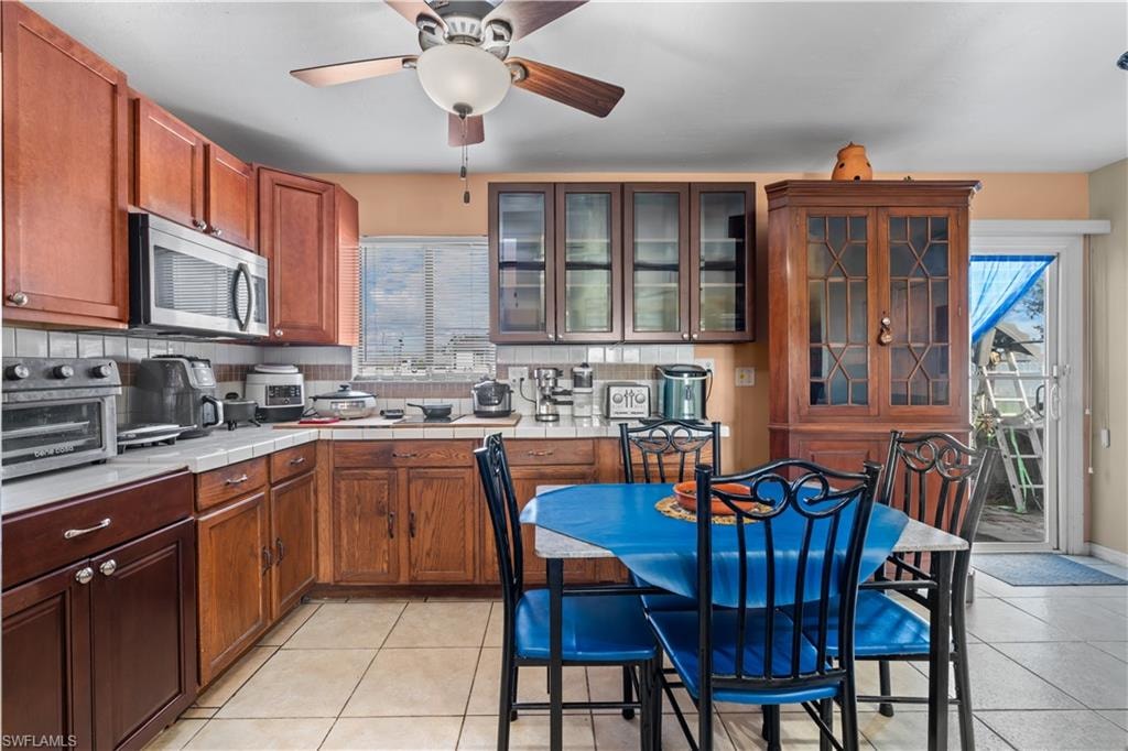 Kitchen with backsplash, light tile patterned floors, stainless steel microwave, and tile counters