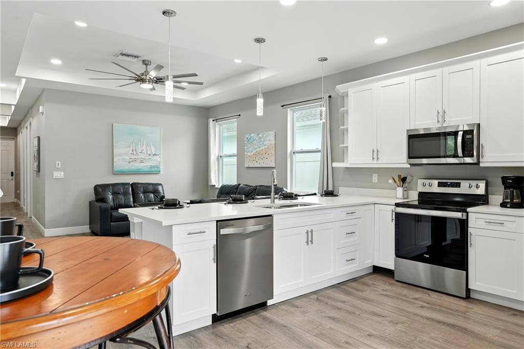 Kitchen with appliances with stainless steel finishes, open floor plan, white cabinets, recessed lighting, and light wood-style floors