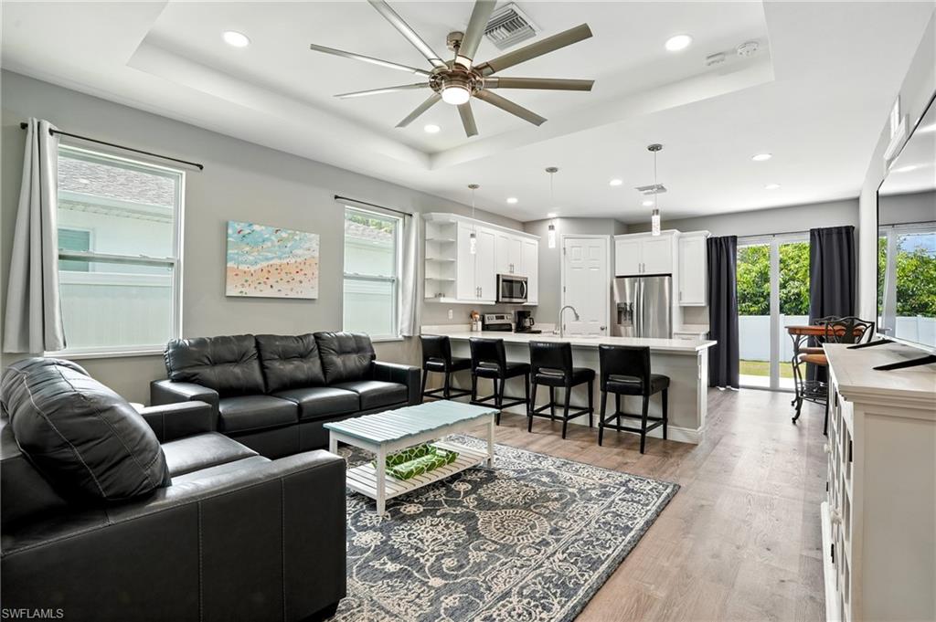 Living area featuring a raised ceiling, light wood-style floors, a ceiling fan, and recessed lighting