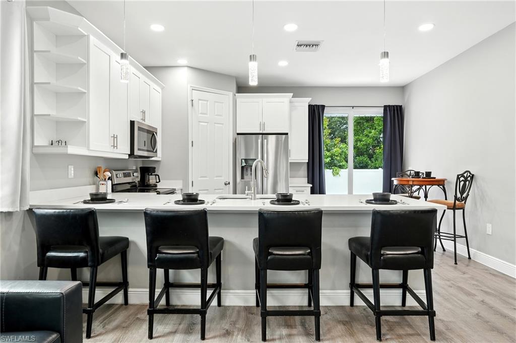 Kitchen with a peninsula, open shelves, white cabinets, light wood-style flooring, and recessed lighting