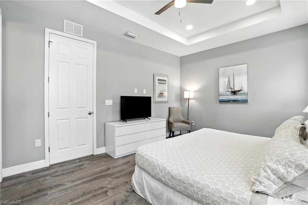 Bedroom with wood finished floors, a tray ceiling, ceiling fan, and recessed lighting