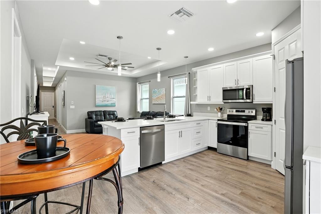 Kitchen featuring open floor plan, a raised ceiling, appliances with stainless steel finishes, pendant lighting, and light wood-style floors