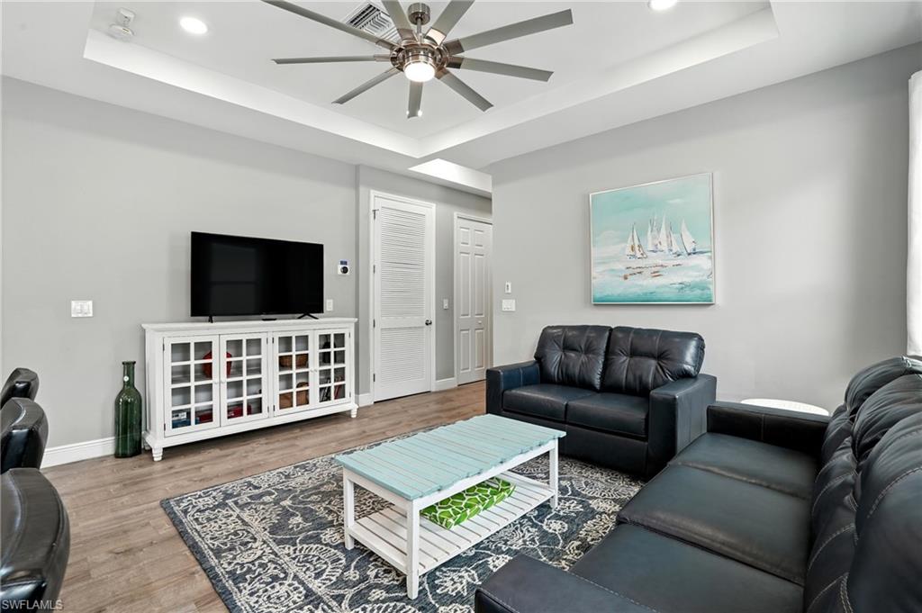 Living room with a raised ceiling, wood finished floors, recessed lighting, and ceiling fan