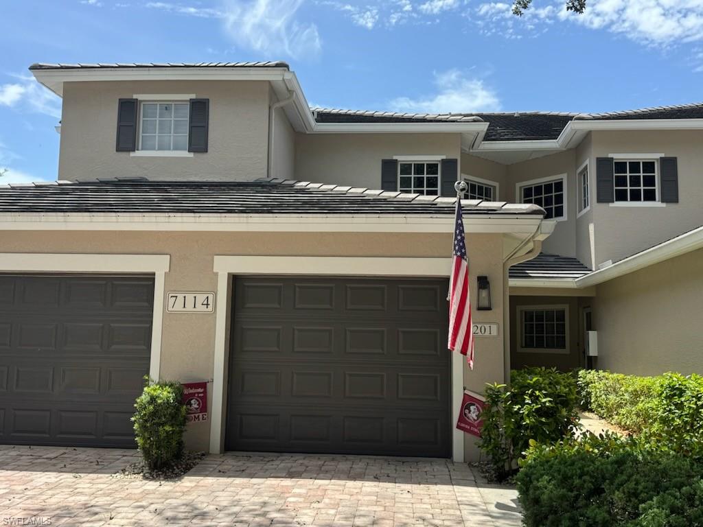 Traditional home with an attached garage, stucco siding, driveway, and a tile roof