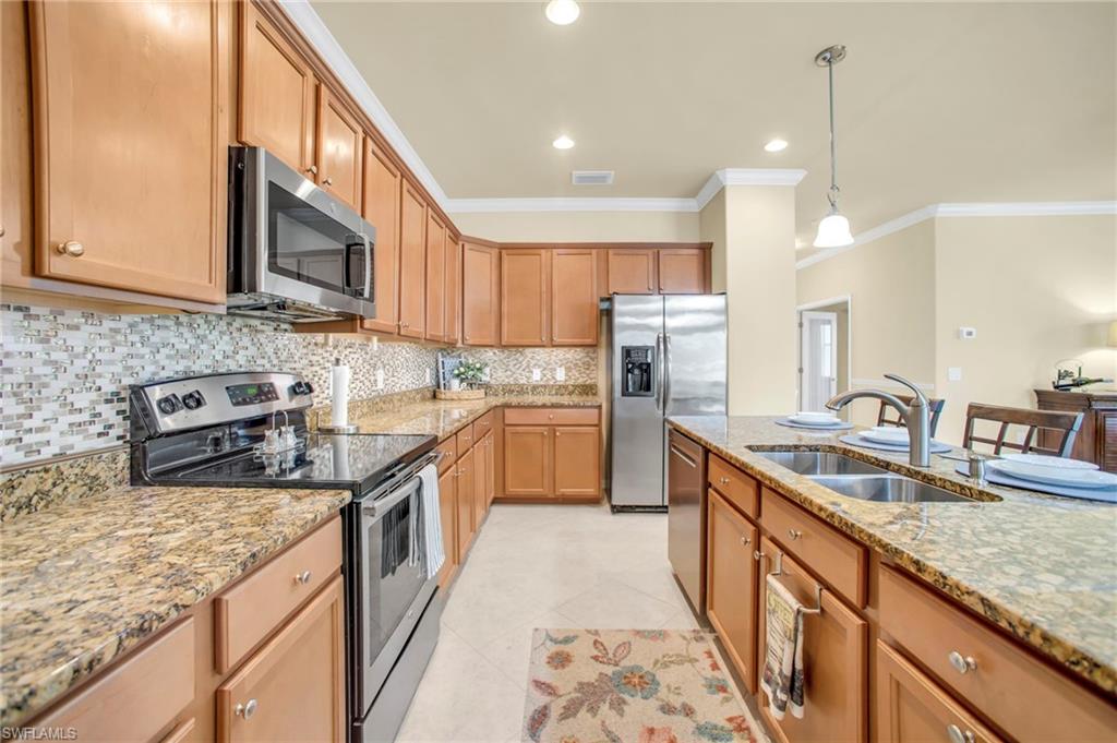 Kitchen with stainless steel appliances, pendant lighting, backsplash,  stone counters, and crown molding