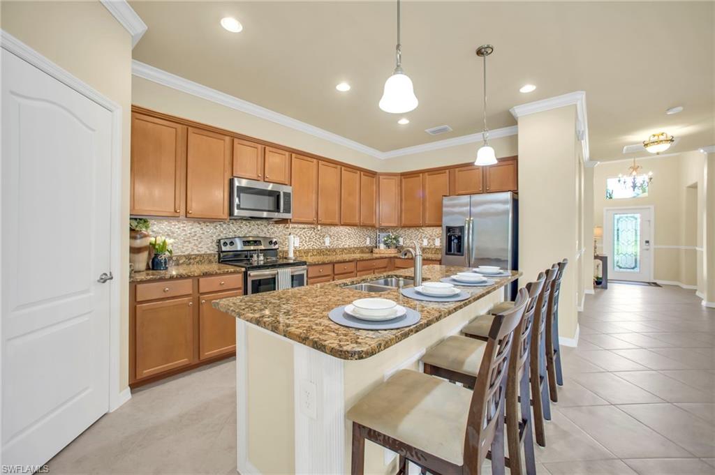 Kitchen with brown cabinetry, a kitchen breakfast bar, tasteful backsplash, decorative light fixtures, and appliances with stainless steel finishes
