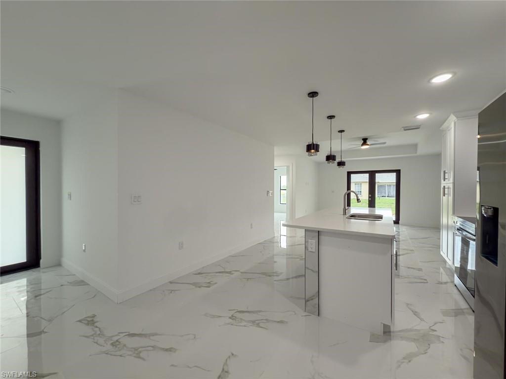Kitchen with light marble finish flooring, a kitchen island with sink, white cabinetry, recessed lighting, and pendant lighting
