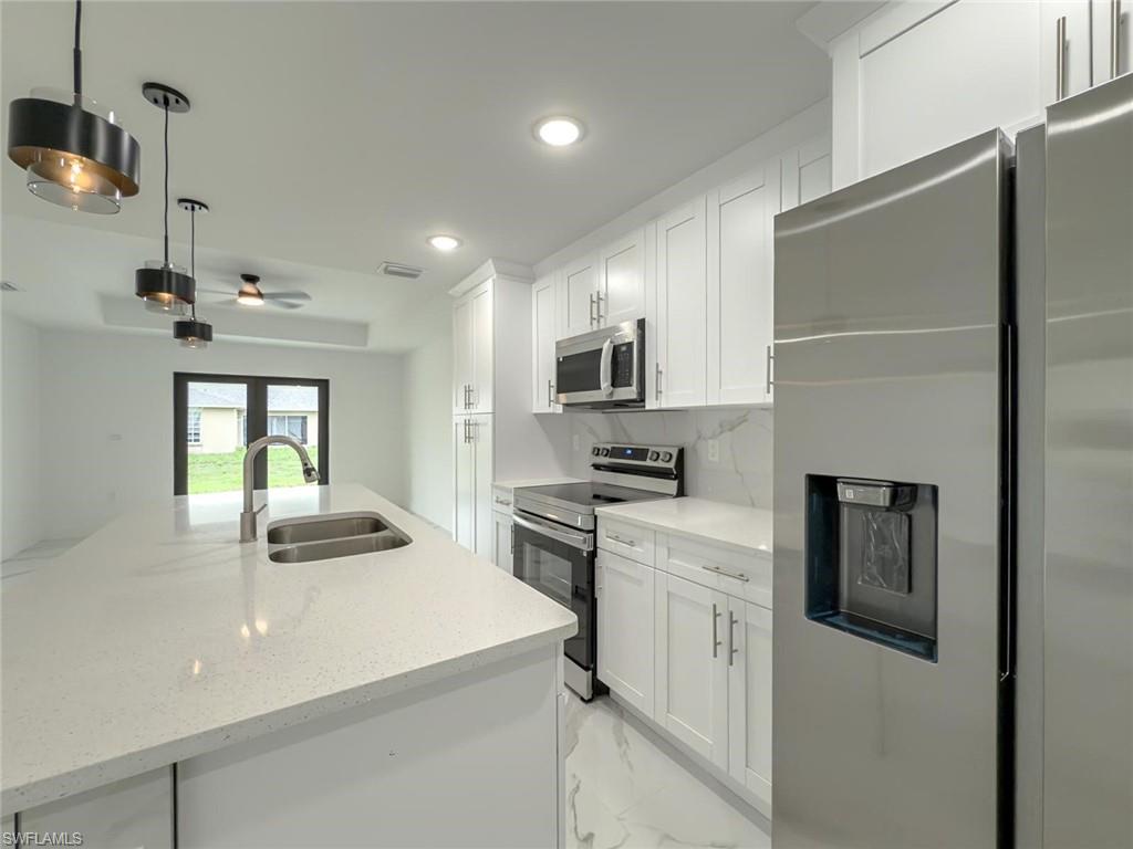 Kitchen featuring appliances with stainless steel finishes, white cabinets, recessed lighting, light stone countertops, and light marble finish floors