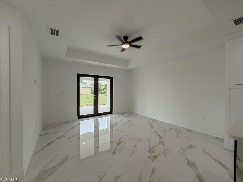 Unfurnished room with light marble finish floors, a tray ceiling, french doors, and ceiling fan