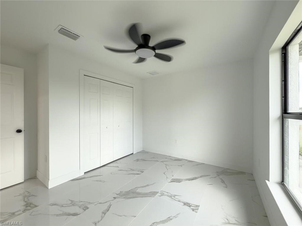 Unfurnished bedroom with light marble finish flooring, a ceiling fan, and a closet