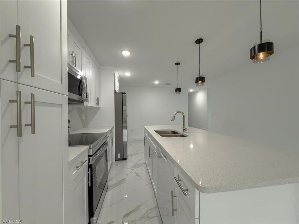 Kitchen with a large island with sink, stainless steel appliances, pendant lighting, light stone counters, and white cabinetry
