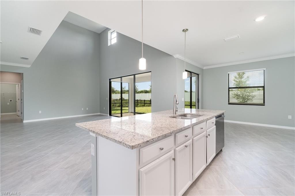 Kitchen with light stone counters, hanging light fixtures, white cabinetry, open floor plan, and an island with sink