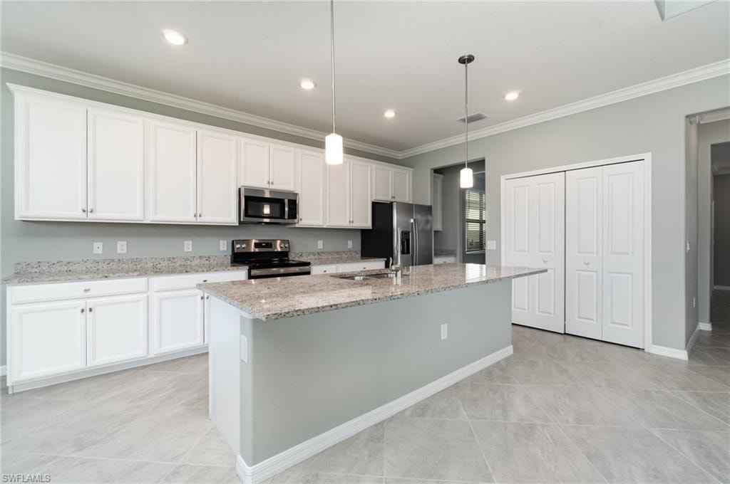 Kitchen with ornamental molding, light stone countertops, appliances with stainless steel finishes, white cabinetry, and a center island with sink