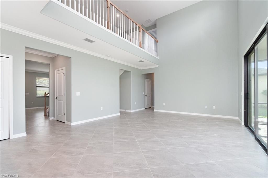 Unfurnished living room featuring a high ceiling, light tile patterned floors, and crown molding