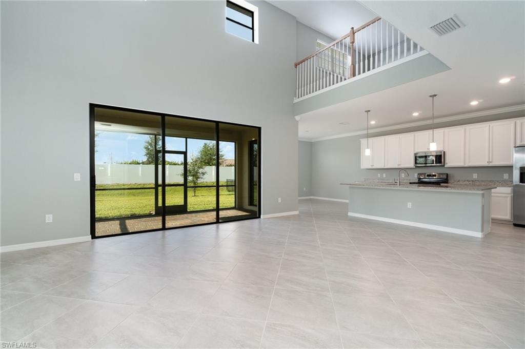 Unfurnished living room with plenty of natural light, a high ceiling, light tile patterned floors, ornamental molding, and recessed lighting