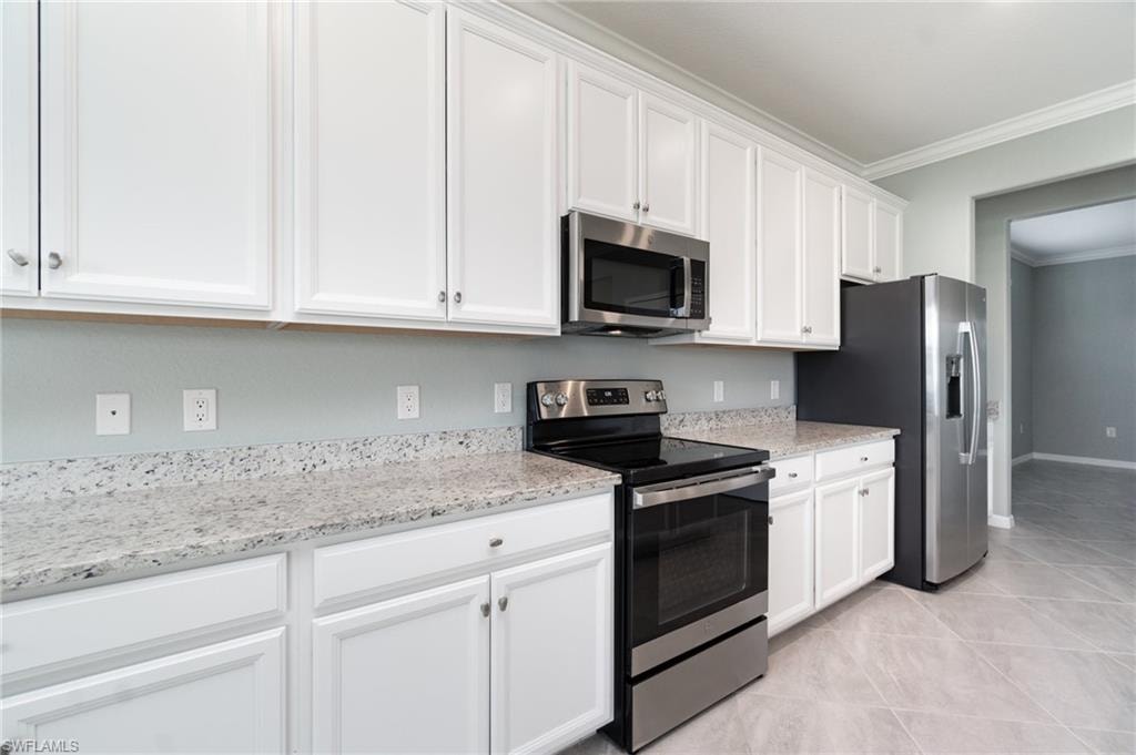 Kitchen featuring stainless steel appliances, white cabinets, light stone counters, ornamental molding, and light tile patterned flooring