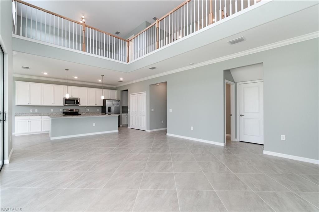 Unfurnished living room with a towering ceiling, ornamental molding, light tile patterned floors, and recessed lighting