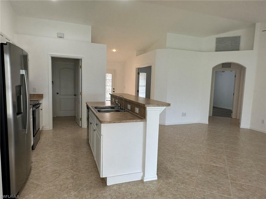 Kitchen with appliances with stainless steel finishes, white cabinets, arched walkways, recessed lighting, and an island with sink