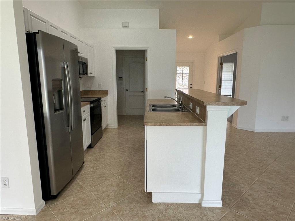 Kitchen with stainless steel appliances, white cabinets, light tile patterned flooring, recessed lighting, and a breakfast bar