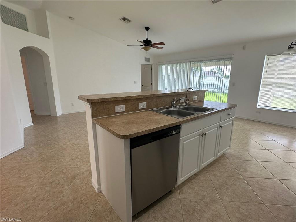 Kitchen featuring white cabinetry, a kitchen island with sink, stainless steel dishwasher, arched walkways, and light tile patterned flooring