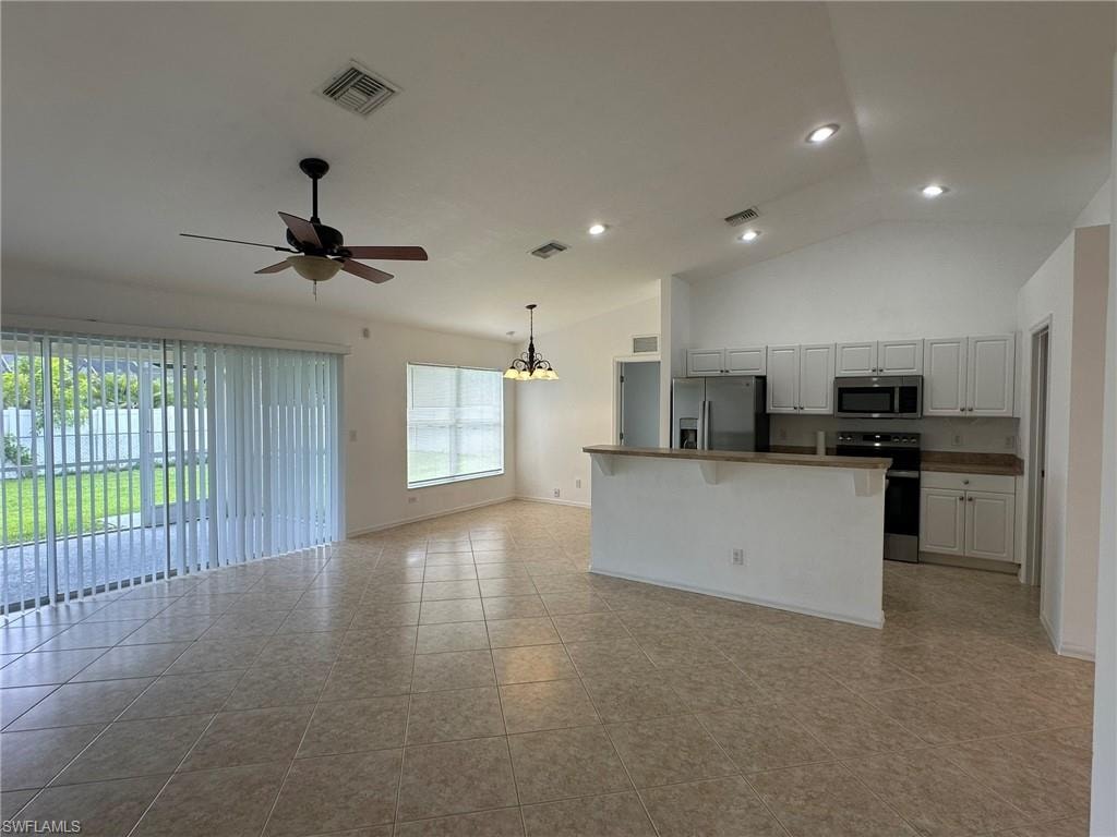 Kitchen with open floor plan, appliances with stainless steel finishes, a chandelier, a kitchen bar, and white cabinets