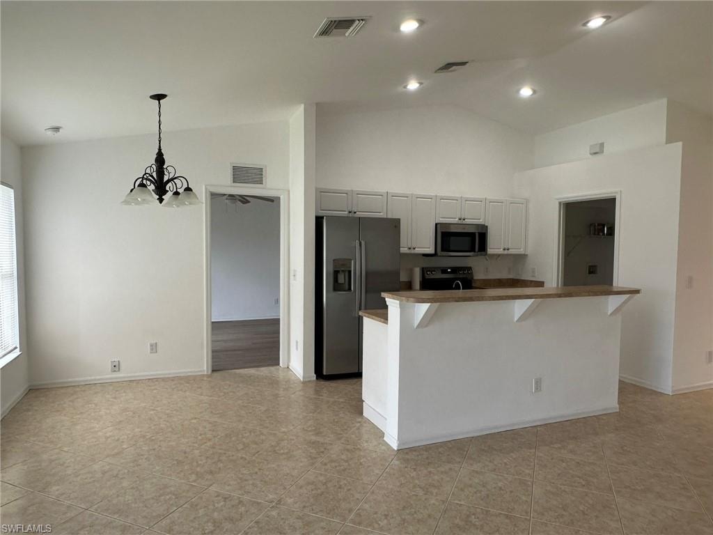 Kitchen featuring stainless steel appliances, a breakfast bar area, decorative light fixtures, a chandelier, and high vaulted ceiling