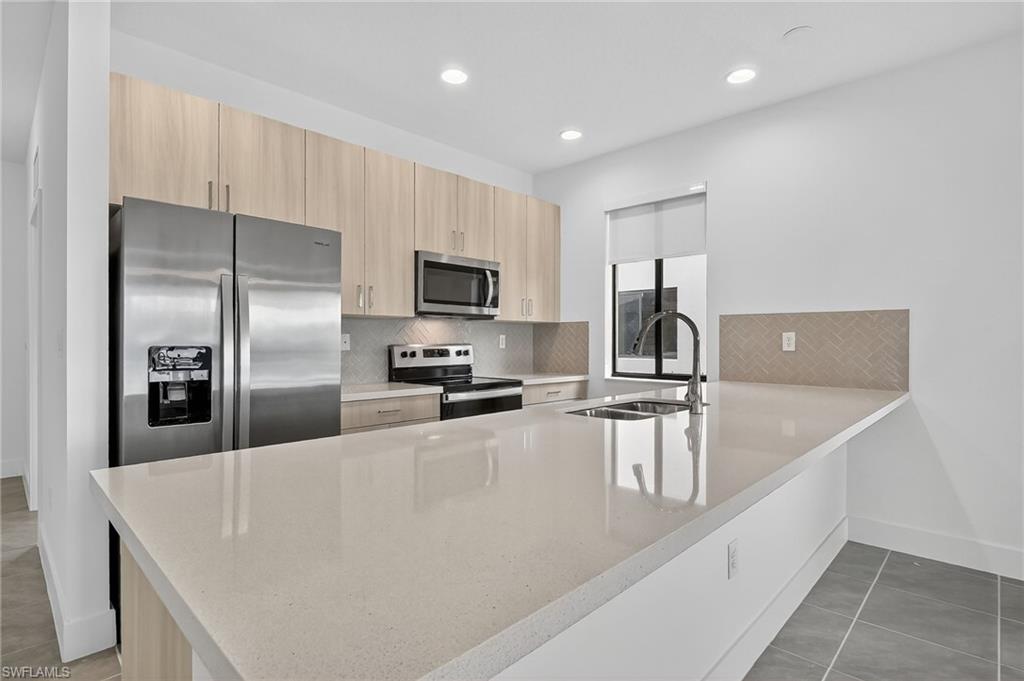 Kitchen with decorative backsplash, a peninsula, light tile patterned flooring, appliances with stainless steel finishes, and recessed lighting