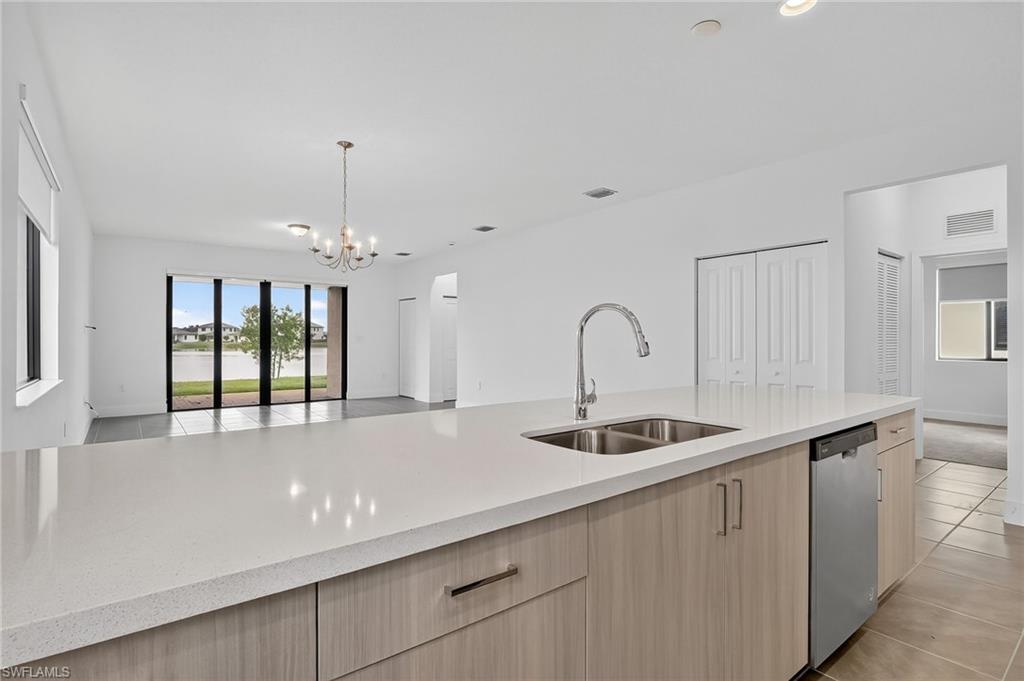 Kitchen featuring light brown cabinetry, open floor plan, light tile patterned floors, light stone counters, and stainless steel dishwasher
