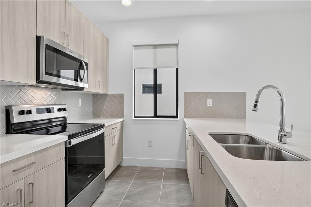 Kitchen with stainless steel appliances, modern cabinets, light tile patterned floors, backsplash, and light brown cabinets