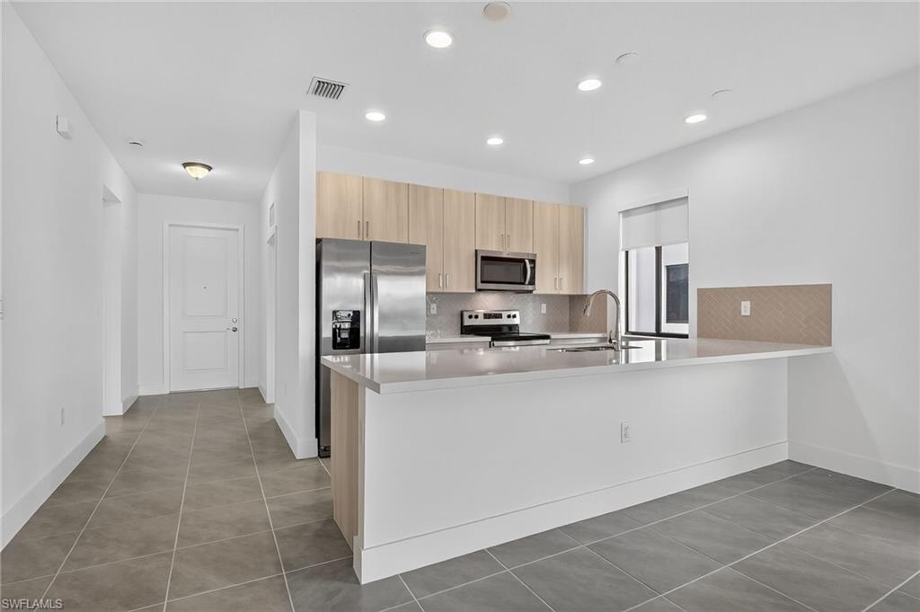 Kitchen featuring light brown cabinets, tasteful backsplash, a peninsula, light tile patterned flooring, and recessed lighting