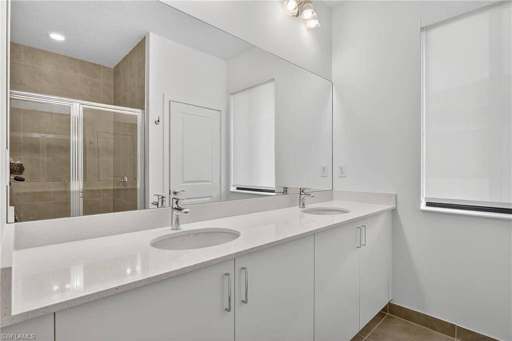 Bathroom featuring double vanity, a stall shower, and dark tile patterned flooring
