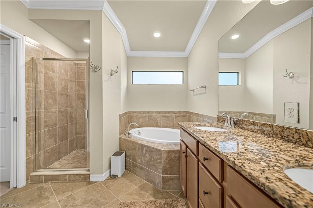 Full bathroom with crown molding, a bath, a shower stall, healthy amount of natural light, and double vanity
