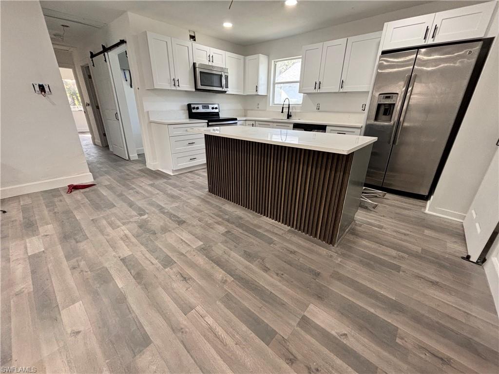 Kitchen featuring a barn door, white cabinets, appliances with stainless steel finishes, a center island, and light wood-type flooring