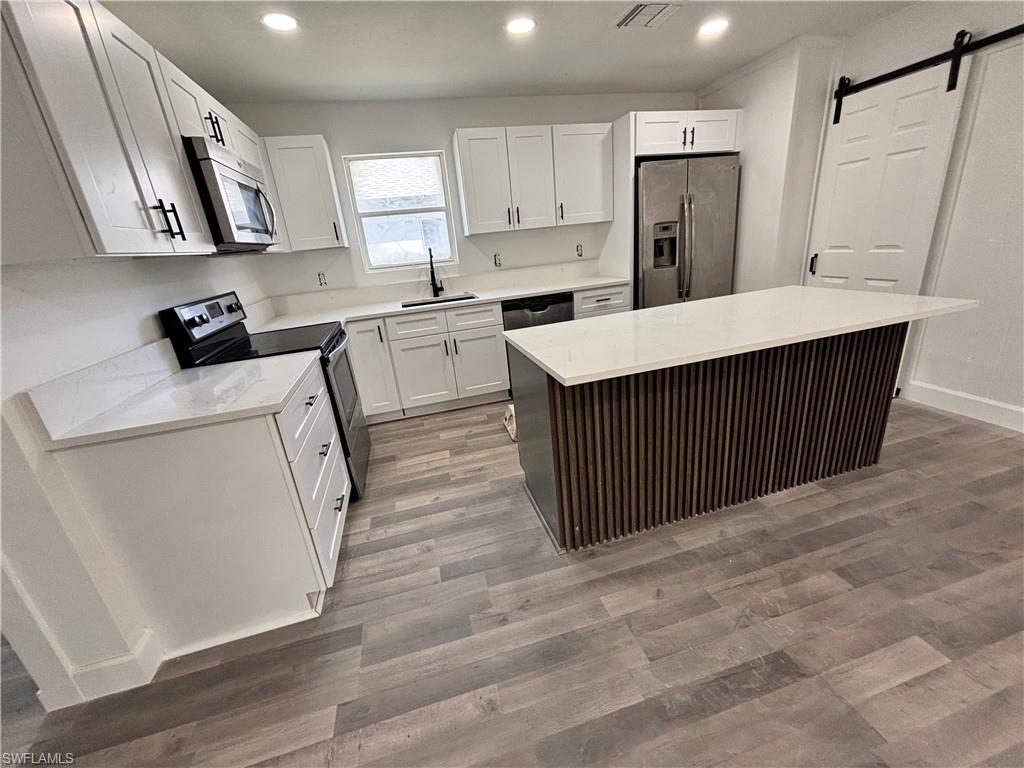 Kitchen featuring a barn door, appliances with stainless steel finishes, light wood-style flooring, white cabinets, and light stone countertops