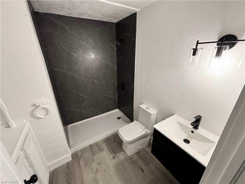 Bathroom featuring a marble finish shower, vanity, wood finished floors, and a textured wall
