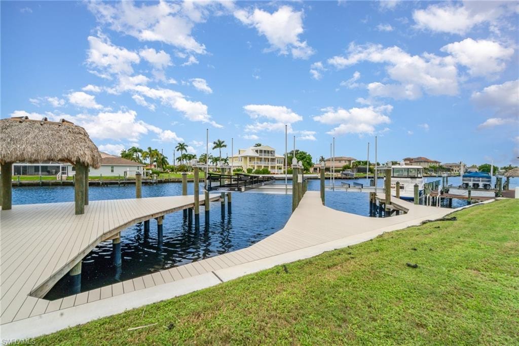 Dock featuring a water view, boat lift, a lawn, and a residential view