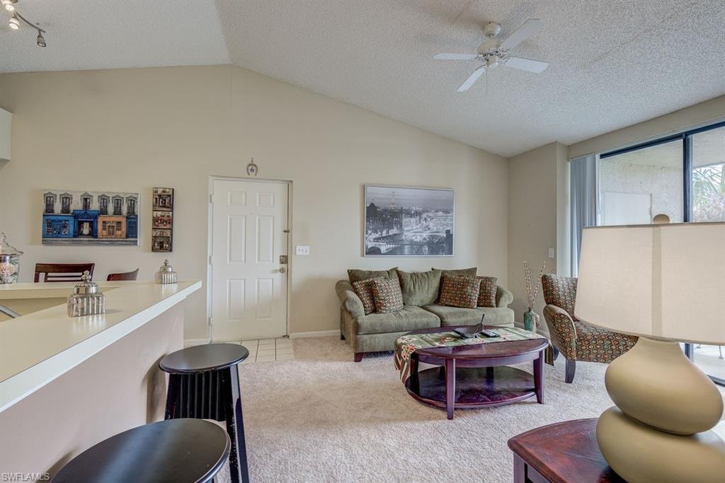 Living area with vaulted ceiling, light carpet, a textured ceiling, ceiling fan, and light tile patterned floors