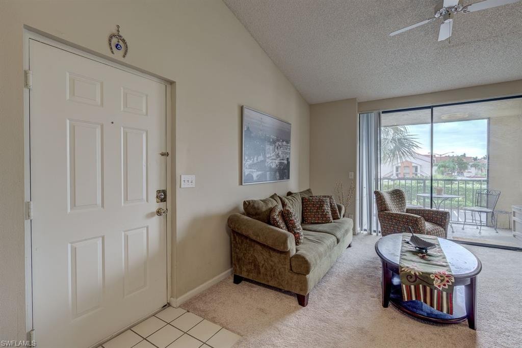 Living area with lofted ceiling, a textured ceiling, light carpet, a ceiling fan, and light tile patterned floors