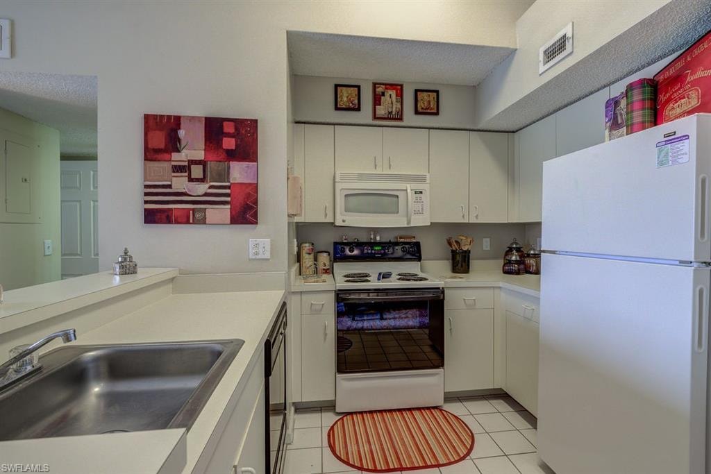 Kitchen with white appliances, light tile patterned floors, light countertops, white cabinets, and a textured ceiling