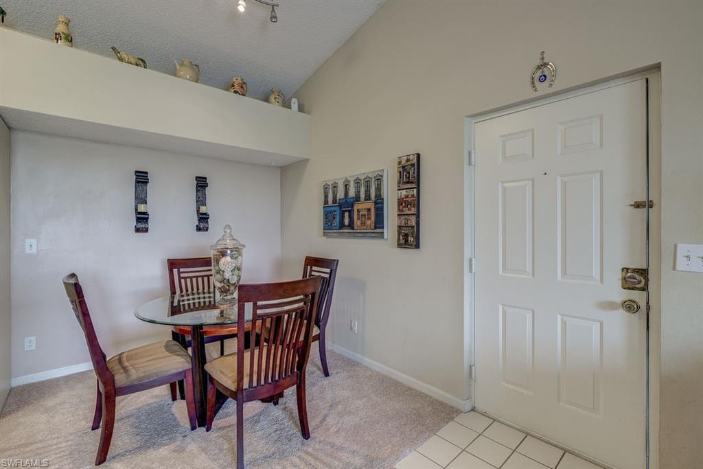 Dining space with light colored carpet, light tile patterned flooring, vaulted ceiling, and a textured ceiling