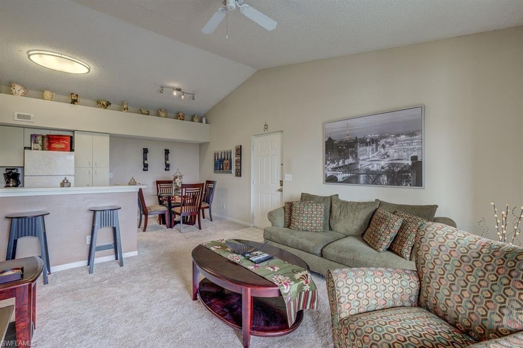 Carpeted living room featuring lofted ceiling, a textured ceiling, and a ceiling fan